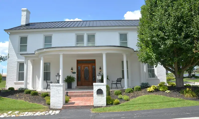 A white-painted brick house with a curved front porch and a standing-seam metal roof
