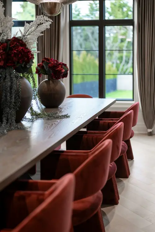 Burgundy velvet dining chairs around a long table with red roses