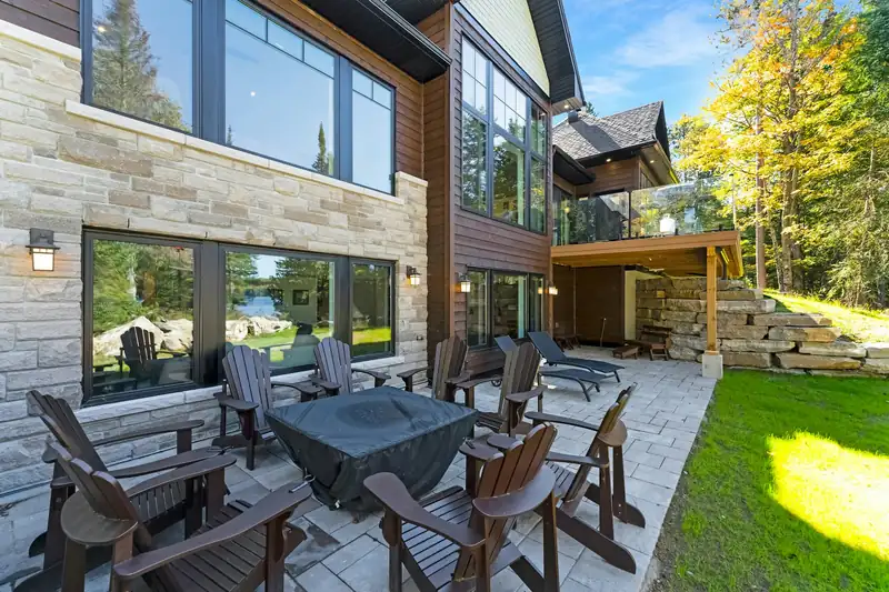 A stone patio with dark wood chairs around a fire pit beside the house